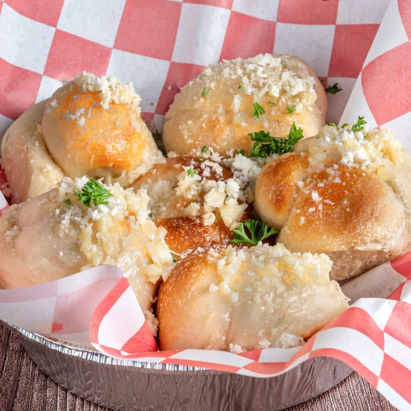 Garlic knots from Mikes Pizza Doral, topped with parmesan cheese and parsley in a foil container.