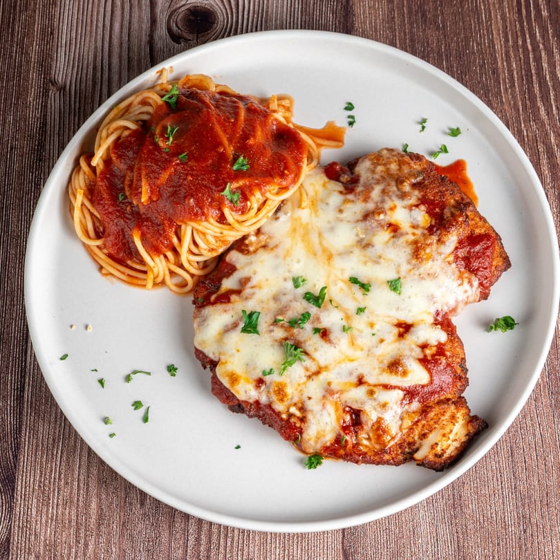 Chicken Parmesan with melted mozzarella and spaghetti with red sauce, garnished with parsley.