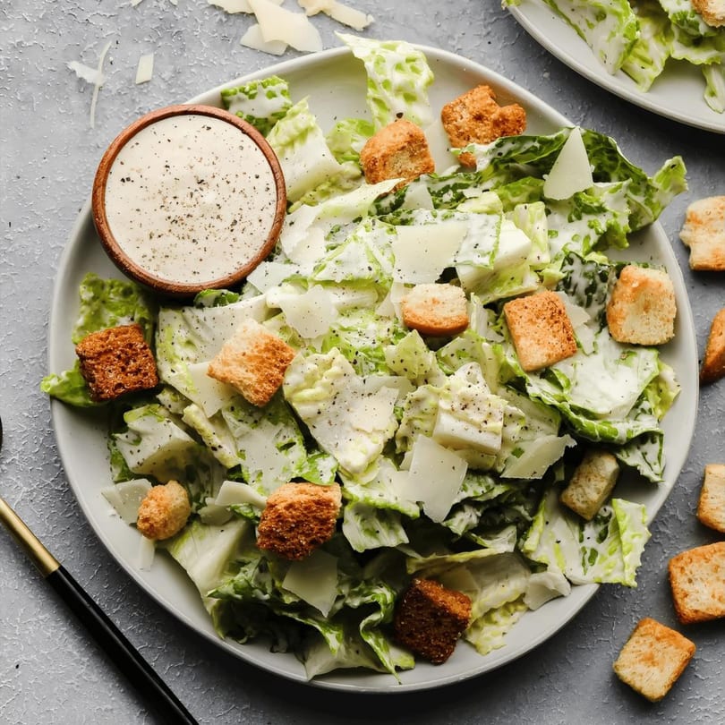 Caesar salad with romaine lettuce, croutons, parmesan cheese, and dressing in a wooden bowl.